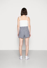 Donna di spalle che indossa un top senza maniche bianco, pantaloni corti a vita alta a scacchi bianco e neri e sneakers alte bianche.