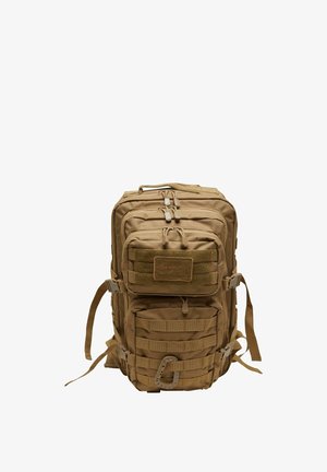 Sac à dos tactique en tissu beige avec de multiples compartiments, zips et sangles pour attaches. Il dispose d'un dos rembourré et de bretelles ajustables.