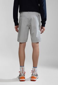 Grå shorts med en glat tekstur, to baglomme og et diskret logo. Bæres med mønstrede sokker og farverige sneakers.
