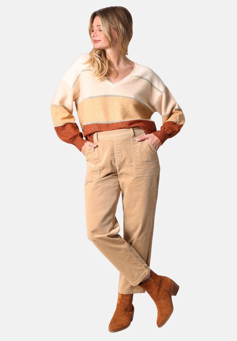 Pull rayé crème et rouille avec un col en V, associé à un pantalon en velours côtelé beige avec des poches latérales, et des bottines marron avec un talon bloc.