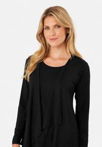 Maglietta nera a maniche lunghe con un davanti drappeggiato. Presenta un colletto rotondo e un tessuto morbido e liscio. Design casual adatto per essere indossato a strati.