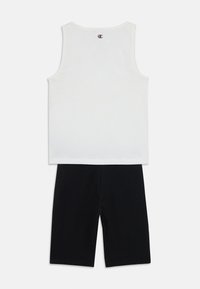 Vit bomullströja utan ärmar med rund halsringning och en liten logotyp på baksidan, tillsammans med svarta bomullsshorts med elastisk midja.