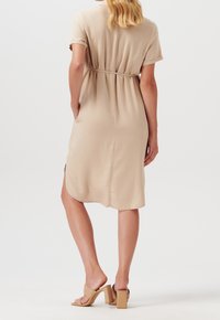 Béžové šaty s krátkým rukávem a páskem v pase, s bočními rozparky a volnou siluetou. V kombinaci s béžovými sandály na platformě.
