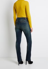Mörkblå skinny jeans med en blekt effekt, med bakfickor och en läderpatch. Matchas med en ljusgul långärmad tröja.