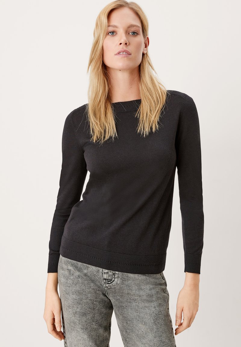 Schwarzer Strickpullover mit langen Ärmeln, rundem Ausschnitt und rippenförmigem Saum und Bündchen, kombiniert mit grauen Jeans aus Denim. Glatte Textur, minimales Design.