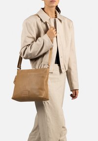 Bruine leren schoudertas met een zachte textuur, rechthoekige vorm en verstelbare schouderriem, voorzien van een subtiele logo-detail.