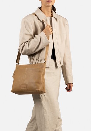 Sac à épaule en cuir tan avec une texture douce, de forme rectangulaire et une bandoulière ajustable, présentant un détail de logo subtile.