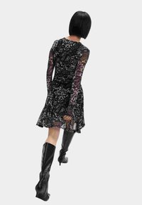 Abito nero a fantasia con maniche lunghe e trasparenti e gonna svasata, abbinato a stivali neri con tacco alto fino al ginocchio. Tessuto liscio, dettagli sulle maniche.