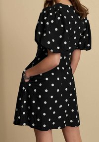 Abito nero con pois bianchi, maniche corte a palloncino e tasche. Il tessuto sembra leggero con una trama liscia.