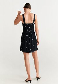 Robe noire avec un corsage ajusté smocké, des bretelles épaisses et une broderie florale. La jupe est fluide avec une silhouette ample, longueur mi-cuisses.
