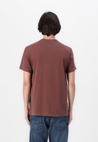 Tricou din bumbac maro cu mâneci scurte și gât rotund, având un design simplu, fără niciun tip de model sau detalii de hardware vizibile.