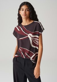 Korte mouwen bordeauxrode en zwarte top met abstracte witte patronen. Gemaakt van soepele stof, heeft het een ontspannen pasvorm en een ronde halslijn.