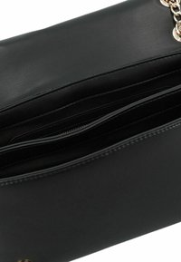 Interno di una borsa a mano in pelle sintetica nera con molteplici scomparti e una texture liscia. Presenta un accento in catena dorata e dettagli con cerniera.