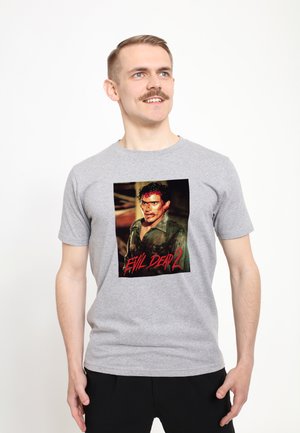 Grå bomuld T-shirt med et centralt motiv af en figur fra "Evil Dead 2" med røde detaljer. Rund hals, korte ærmer, løs pasform.