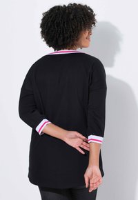 Sort langærmet skjorte med rund hals. Manchetterne har hvide og pink striber. Blødt stof med en afslappet pasform og slidser i siderne.