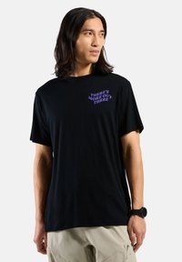 Schwarzes Baumwoll-T-Shirt mit kurzen Ärmeln und Rundhalsausschnitt. Text in lila mit der Aufschrift "DA DRAUSSEN GIBT ES MEHR" auf der linken Brustseite.