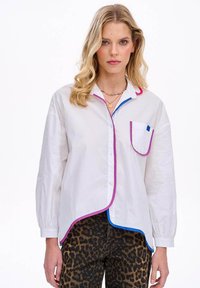 Biała koszula z guzikami, ozdobiona różowymi i niebieskimi detalami, z jedną kieszenią z niebieskim akcentem kwadratowym. Długie rękawy i luźny krój.