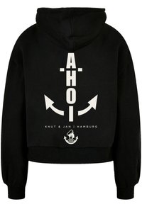 Black hooded sweatshirt featuring a large white "AHOI" text, arrows, and nautical motifs printed on the back. Ribbed cuffs and hem.