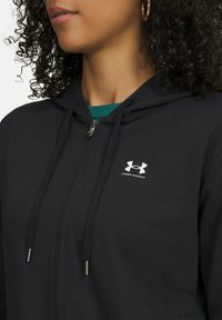 Felpa nera con zip, realizzata in tessuto strutturato, con un piccolo logo bianco Under Armour, chiusura con coulisse e cappuccio incorporato.