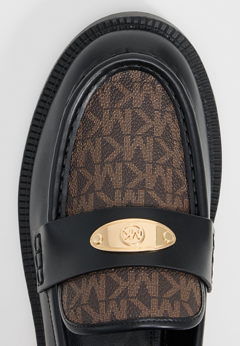 Leren instappers met bruine MK-monogram stof, zwarte leren afwerking en gouden ovale logo plaat op de band.