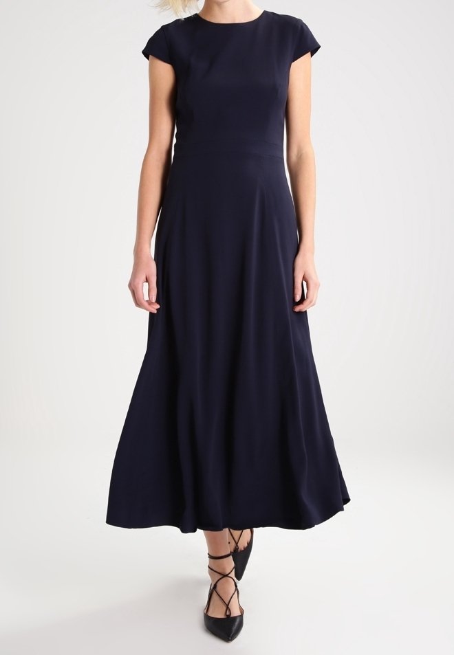 Femme portant une robe bleu marine à manches courtes, longueur cheville, avec des ballerines noires à bout pointu et des brides croisées aux chevilles.