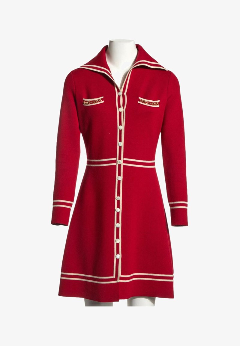Robe rouge à manches longues boutonnée avec bordure blanche, grand col, deux poches poitrine avec détail chaîne et taille cintrée sur un mannequin.