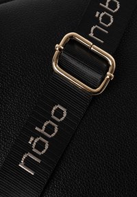 Borsa a tracolla nera in ecopelle con superficie texturizzata, tracolla piana nera con fibbia dorata e il nome del marchio "nöbo" in argento.