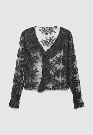 Blouse en dentelle noire avec un motif floral, col en V et manches longues. Tissu transparent avec broderie texturée et poignets à volants.