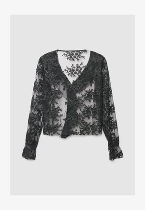 Blouse en dentelle noire avec un motif floral, col en V et manches longues. Tissu transparent avec broderie texturée et poignets à volants.