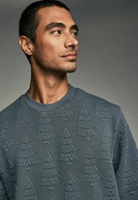 Gray sweatshirt featuring a textured pattern of pine trees, crew neckline, and ribbed cuffs. Material appears soft and thick.