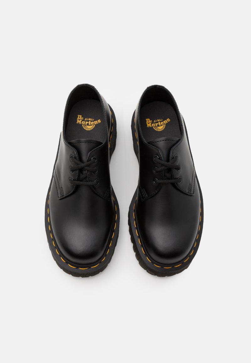 Scarpe stringate in pelle nera con punta tonda, cuciture gialle e suola nera spessa e distintiva. L'interno presenta una soletta nera con logo.