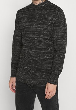Schwarzer Pullover mit hohem Kragen, der ein strukturiertes Muster und feine silberne Fäden aufweist, aus einem weichen, gemischten Stoff gefertigt.