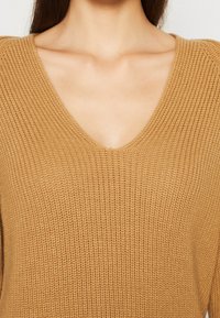 Maglione lavorato a maglia marrone chiaro con scollo a V e tessuto testurizzato, che mette in risalto il motivo a punto e i dettagli a costine.