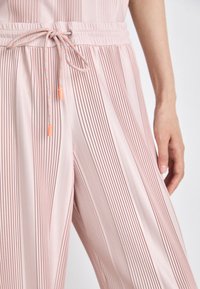 Rosa gefaltete Hosen verfügen über einen elastischen Bund mit einem verstellbaren Kordelzug, der mit orangenen Spitzen versehen ist. Die weiche, glatte Textur erhöht den Komfort.