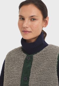 Sivi teksturirani flis prsluk s rebrastim mornarskosinjim turtleneck ovratnikom, zelenim gumbima i tamnim gumbima. Glatka tkanina kontrasta na rukavima.