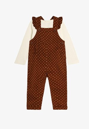 Rudos kordūrinės petnešos su baltomis taškeliais, su raukšlėmis ant dirželių, kvadratiniais iškirpimais ir sagomis ant pečių; derinamos su baltu marškinėliu.