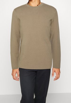 Langärmliger Pullover mit Rundhalsausschnitt in neutralem Taupe. Hergestellt aus weichem, strukturiertem Stoff mit lockerer Passform. Kombiniert mit dunklen, schmal zulaufenden Hosen.