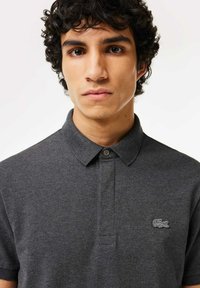 Mörkgrå pikétröja i mjukt tyg, med krage, knappslå och en liten broderad logo på bröstet.