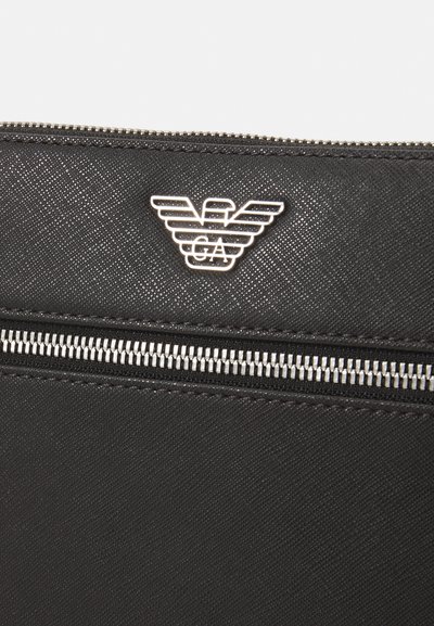 Black textured fabric clutch with a silver zipper and a raised eagle logo. The design is sleek and modern, featuring a matte finish.
