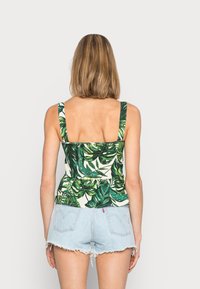 Top de alças largas com padrão de folhas verdes, corpo ajustado e barra peplum, combinado com calções de ganga claros, com bordas desfiadas.