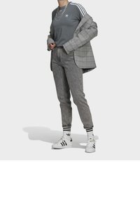 Grå träningsöverdel med vita tre ränder, rutigt kavaj, grå byxor, vita sneakers med svarta ränder, och randiga strumpor med logotyper.