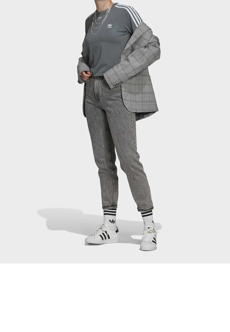 Grå träningsöverdel med vita tre ränder, rutigt kavaj, grå byxor, vita sneakers med svarta ränder, och randiga strumpor med logotyper.