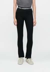 Juodos leggingai, pagaminti iš elastingos medžiagos, su prigludusia forma ir platėjančiomis apačiomis. Turi plačią juosmenį su užrašu "KARL LAGERFELD JEANS".