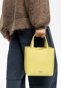 Żółta skórzana torebka z dwoma krótkimi uchwytami. Gładka faktura i minimalistyczny design. Logo wytłoczone na przodzie. Rozmiar: mały i kompaktowy.