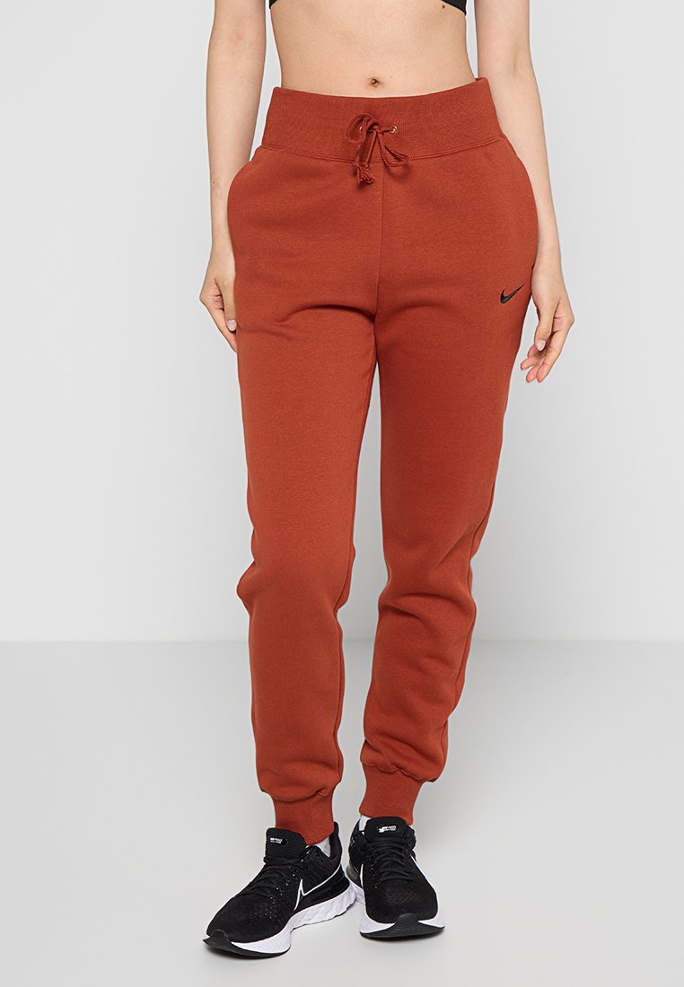 Pantalons de jogging Nike en orange rouille, avec une taille à cordon, des jambes fuselées, des poignets côtelés et un petit logo noir sur la cuisse gauche.