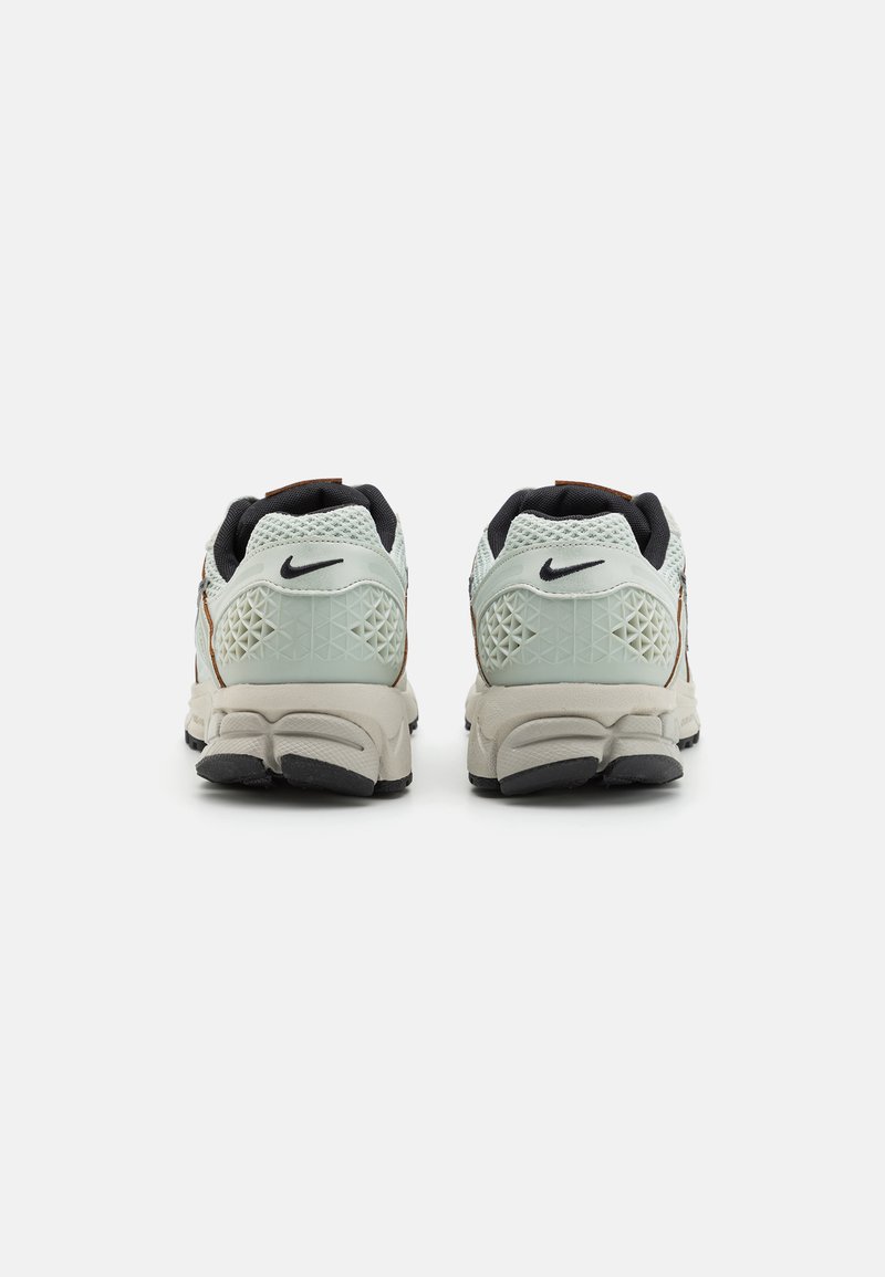 Chaussures de course Nike avec une tige en mesh vert clair, des accents à motif en diamant, des détails noirs et une semelle rembourrée avec une base grise et un profil noir.