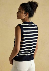 Tumesinise ja valge triibuline ilma varrukateta sviiter, millel on soonikkoes kaelus ja äär. Pehme kangas ja mugav lõige, kantud valgete pükste üle.