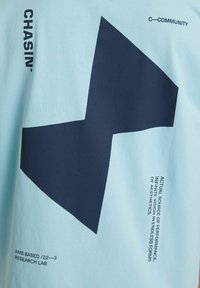 Hellblaues Baumwoll-T-Shirt mit einem großen dunkelblauen geometrischen Design, auf dem Ärmel und der unteren Vorderseite sind gedruckte Texte.
