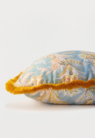 Coussin décoratif bleu avec des motifs floraux complexes en orange et jaune, bordé d'une épaisse frange jaune moutarde.