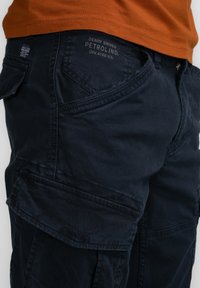 Marineblauwe cargo pants met meerdere zakken, met een soepele textuur en gestikte details. Merketiket zichtbaar op de tailleband.